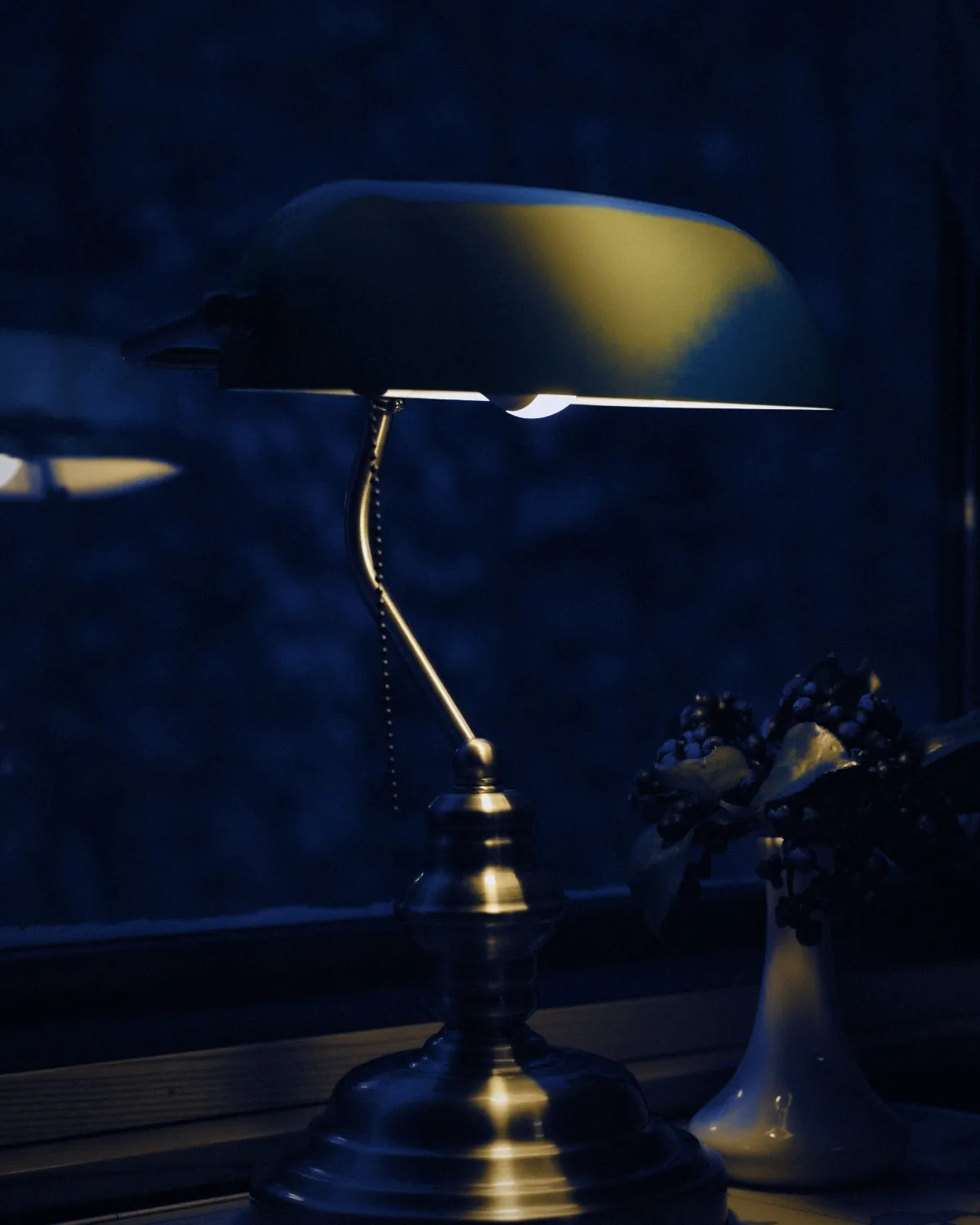 A brass desk lamp by a window at dusk